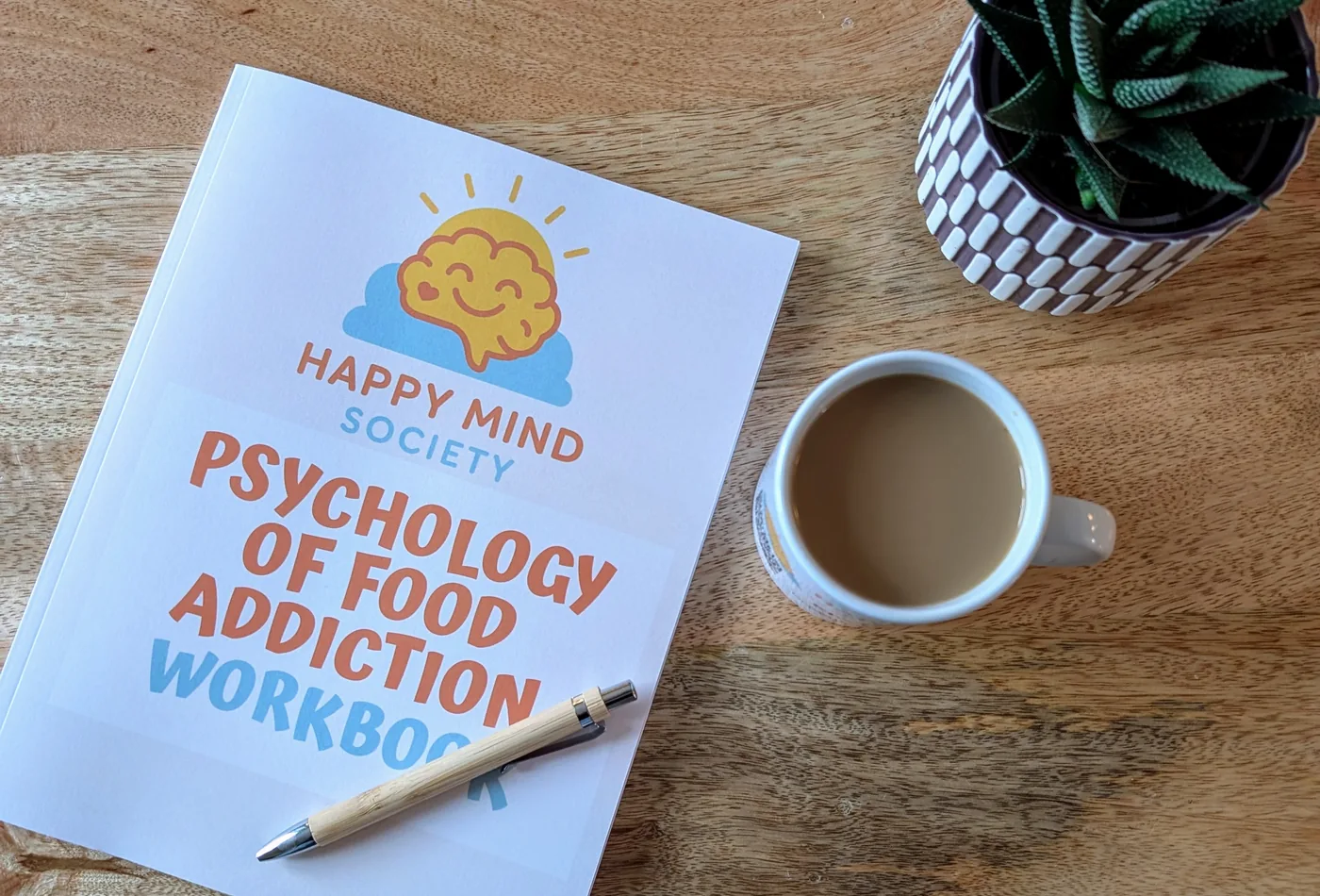 Happy Mind Society printed workbook on a table with a pen, plant, and cup of tea